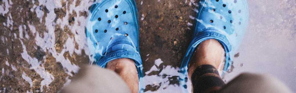 Person steht in knöcheltiefem Wasser und trägt blaue Clogs.